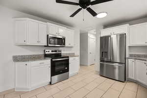 Kitchen with stainless steel appliances, white cabinetry, light stone counters, ceiling fan, and light tile patterned floors