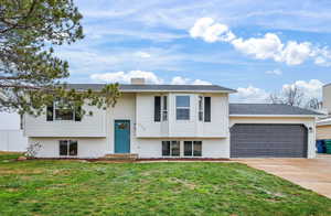Split foyer home with brick siding, a front yard, concrete driveway, an attached garage, and a chimney