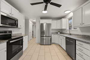 Kitchen with appliances with stainless steel finishes, white cabinets, light stone countertops, and a ceiling fan