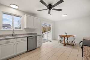 Kitchen with stainless steel dishwasher, light stone counters, plenty of natural light, and white cabinetry