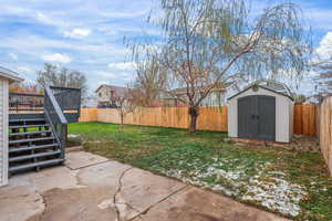 Fenced backyard featuring a deck, a storage shed, stairs, and a patio