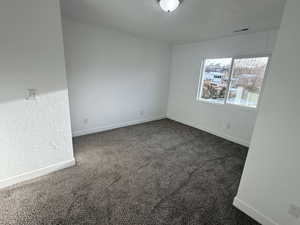 Unfurnished room featuring dark colored carpet and a textured wall