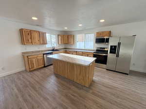 Kitchen featuring appliances with stainless steel finishes, recessed lighting, a kitchen island, brown cabinets, and a textured ceiling