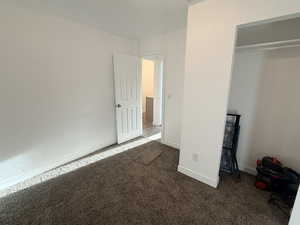 Unfurnished bedroom with dark colored carpet and baseboards