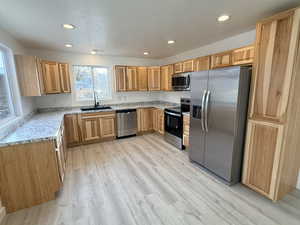 Kitchen featuring stainless steel appliances, recessed lighting, light stone counters, light wood-style floors, and a textured ceiling