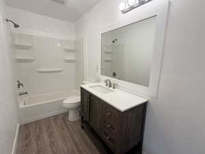 Full bathroom with a textured wall, vanity, dark wood-type flooring, and tub / shower combination