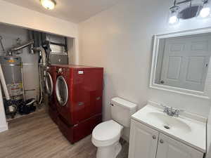 Bathroom featuring washer and dryer, a textured wall, vanity, secured water heater, and light wood-style floors