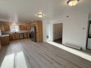 Kitchen with stainless steel appliances, light wood-style floors, stacked washer / drying machine, brown cabinets, and light countertops