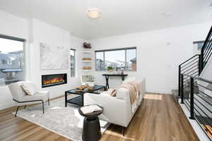 Living area with wood finished floors, a glass covered fireplace, and stairs