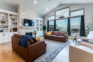 Living room with a stone fireplace, light wood-type flooring, high vaulted ceiling, and recessed lighting