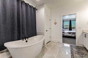 Bathroom with vanity, a freestanding bath, light marble finish floors, and ensuite bathroom