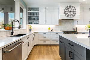 Kitchen featuring stainless steel dishwasher, open shelves, white cabinetry, gray cabinetry, and light stone counters