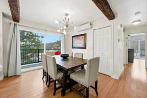 Dining space featuring beam ceiling, a chandelier, light wood-style flooring, and a wall unit AC