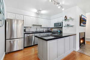 Kitchen featuring a peninsula, white cabinetry, stainless steel appliances, open shelves, and tasteful backsplash