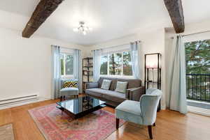 Living area featuring beam ceiling, light wood-style flooring, and a baseboard heating unit