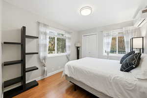 Bedroom featuring an AC wall unit, multiple windows, light wood-type flooring, and a closet