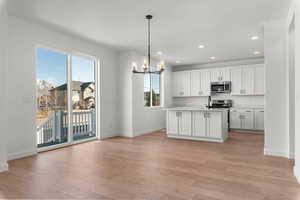 Kitchen with a chandelier, white cabinets, an island with sink, decorative light fixtures, and stainless steel appliances
