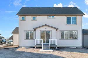 Back of property featuring a shingled roof, stucco siding, and a deck