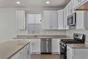 Kitchen with appliances with stainless steel finishes, white cabinets, light wood finished floors, and recessed lighting