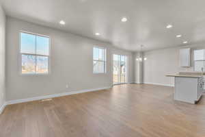 Unfurnished living room with recessed lighting, light wood finished floors, a chandelier, plenty of natural light, and a textured ceiling