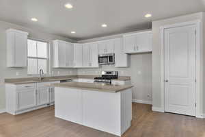 Kitchen with white cabinets, appliances with stainless steel finishes, recessed lighting, light wood finished floors, and light countertops