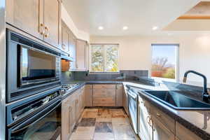 Kitchen featuring black appliances, recessed lighting, stone tile flooring, dark stone counters, and decorative backsplash