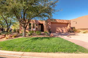 Pueblo-style home featuring driveway, a front yard, a garage, and stucco siding