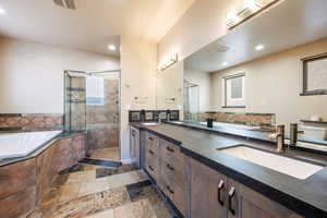 Bathroom featuring a bath, double vanity, a stall shower, stone tile flooring, and recessed lighting