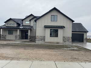 View of front of home featuring stone siding, covered porch, roof with shingles, board and batten siding, and driveway
