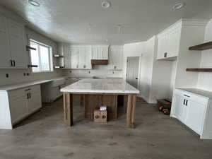 Kitchen with open shelves, a kitchen island, a textured ceiling, white cabinets, and recessed lighting