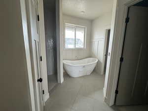 Bathroom featuring a freestanding tub, a decorative wall, a wainscoted wall, light tile patterned flooring, and a textured ceiling