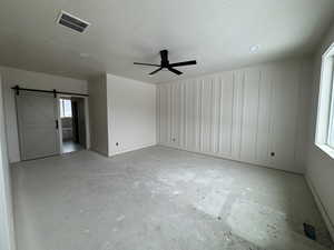 Unfurnished bedroom with a barn door, a ceiling fan, a textured ceiling, unfinished concrete floors, and ensuite bath