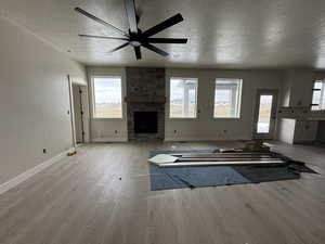Unfurnished living room featuring a textured ceiling, a stone fireplace, light wood-style flooring, and a ceiling fan