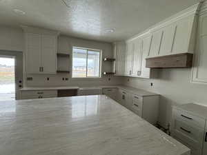 Kitchen featuring white cabinets, a textured ceiling, light stone counters, open shelves, and custom exhaust hood