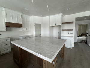 Kitchen with white cabinets, open shelves, a kitchen island, a textured ceiling, and dark wood-style floors