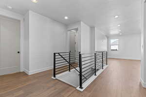 Hall with an upstairs landing, recessed lighting, light wood-style flooring, and a textured ceiling