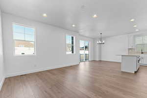 Unfurnished living room with recessed lighting, light wood-style floors, a chandelier, plenty of natural light, and a textured ceiling