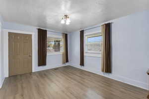 Empty room featuring a textured ceiling, wood finished floors, and a chandelier