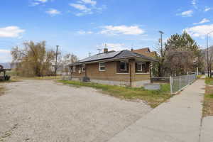 View of property exterior featuring roof mounted solar panels, brick siding, a chimney, and driveway