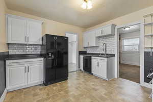 Kitchen featuring black appliances, white cabinets, tasteful backsplash, and dark stone countertops