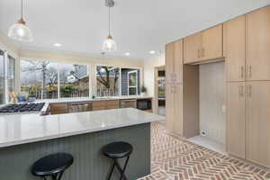 Kitchen with brick floors, a kitchen breakfast bar, light brown cabinetry, hanging light fixtures, and ornamental molding