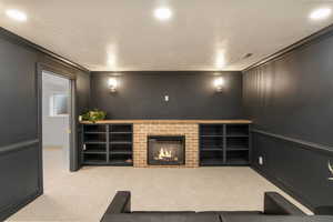 Living area with crown molding, light carpet, a decorative wall, a brick fireplace, and recessed lighting