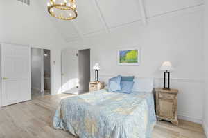 Bedroom featuring high vaulted ceiling, a chandelier, wood finished floors, connected bathroom, and beam ceiling