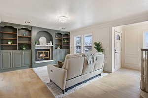 Living area with a decorative wall, wood finished floors, a glass covered fireplace, and built in shelves