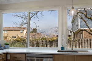 Kitchen view of stainless steel dishwasher, hanging light fixtures, and light stone countertops