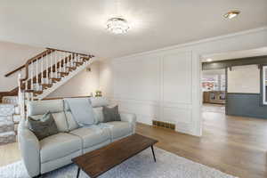 Living area featuring a decorative wall, light wood-type flooring, stairs, and ornamental molding