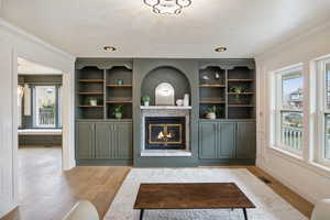 Living area with a glass covered fireplace, light wood-style flooring, and ornamental molding