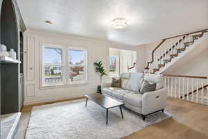 Living area with light wood-type flooring, a textured ceiling, stairway, and ornamental molding