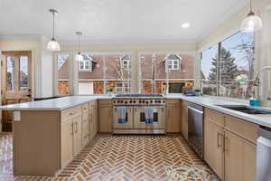 Kitchen with hanging light fixtures, brick flooring, appliances with stainless steel finishes, a peninsula, and light brown cabinets