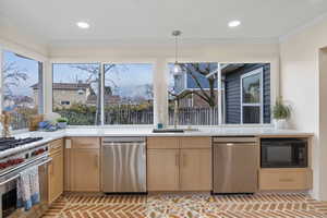 Kitchen featuring light brown cabinets, appliances with stainless steel finishes, pendant lighting, healthy amount of natural light, and crown molding